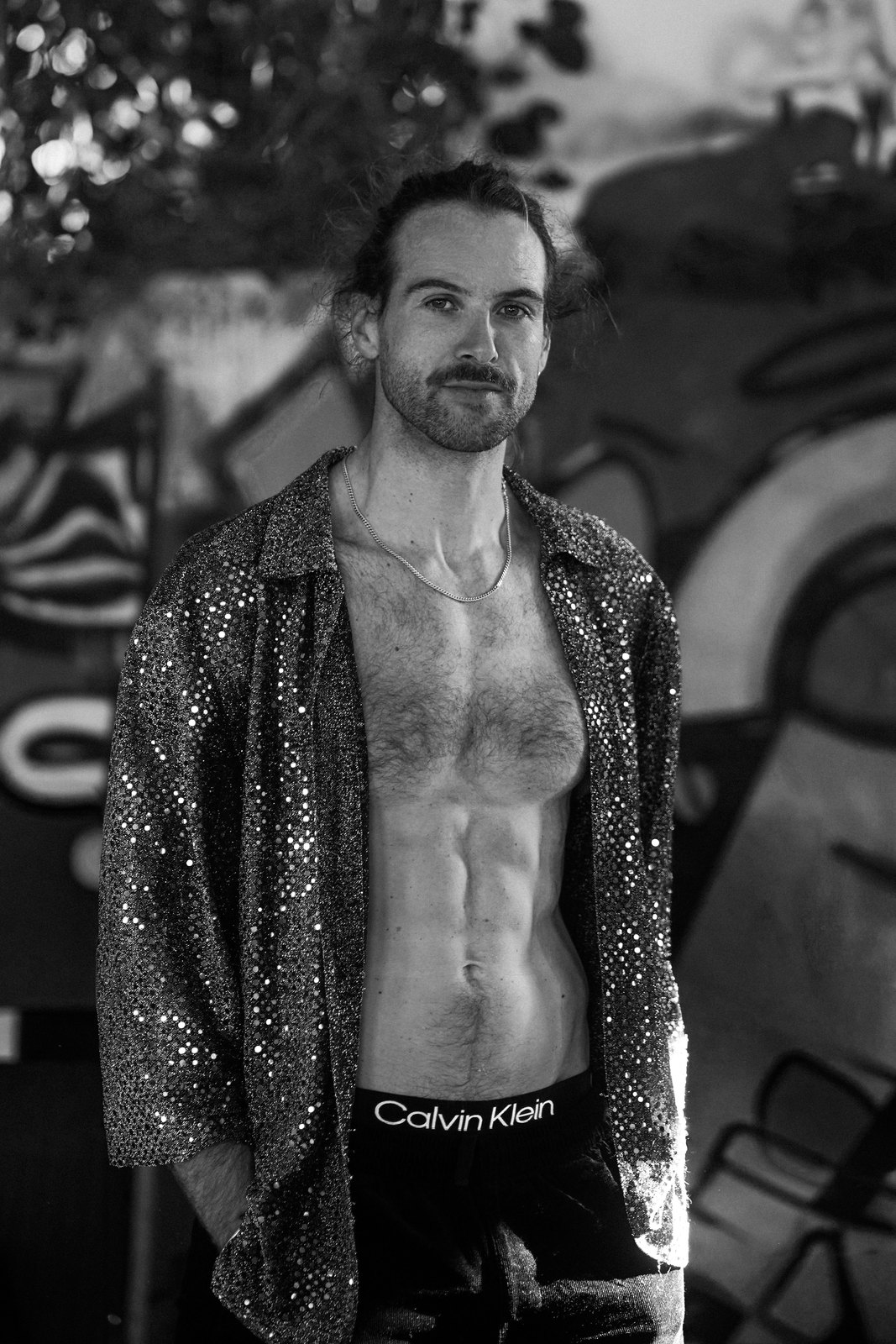 Black and white portrait of a man in a sequin shirt in front of graffiti