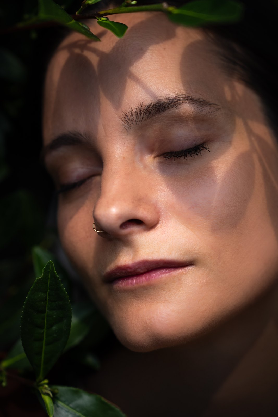 Close portrait of a woman with closed eyes and leaf shadows