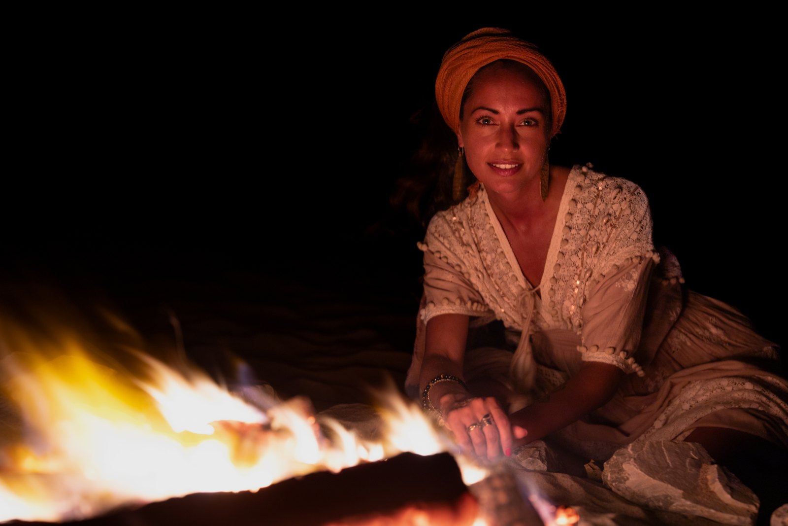 Woman in a headscarf smiling beside a campfire at night