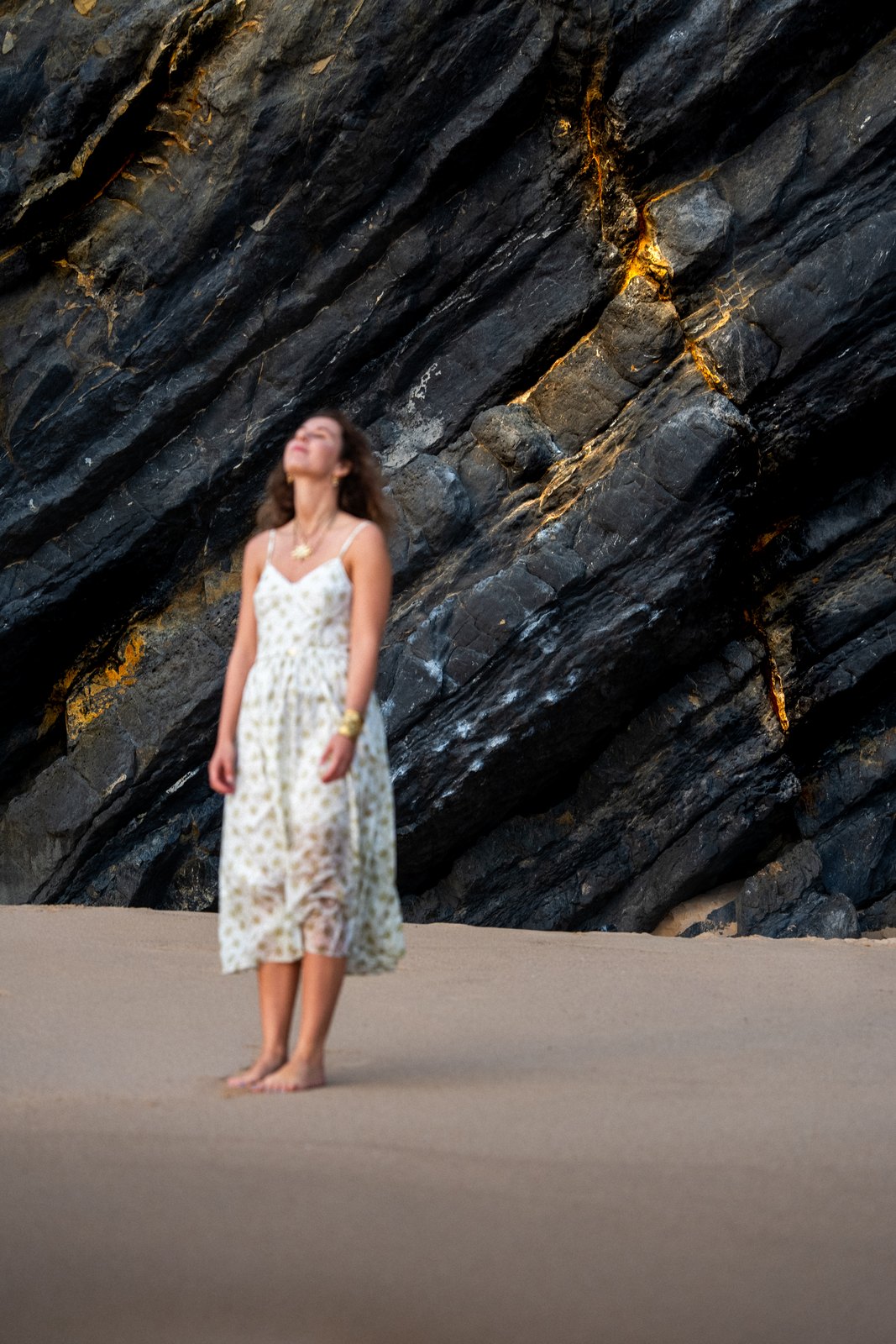 Woman in a white dress against dark cliffs on the beach