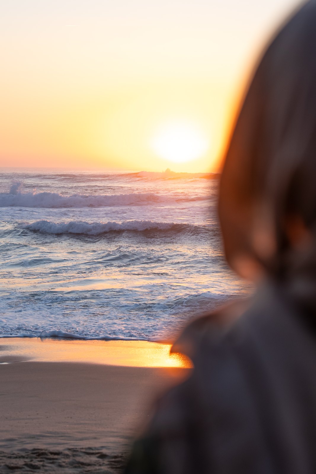 Looking past a woman's shoulder at the sun setting over the sea