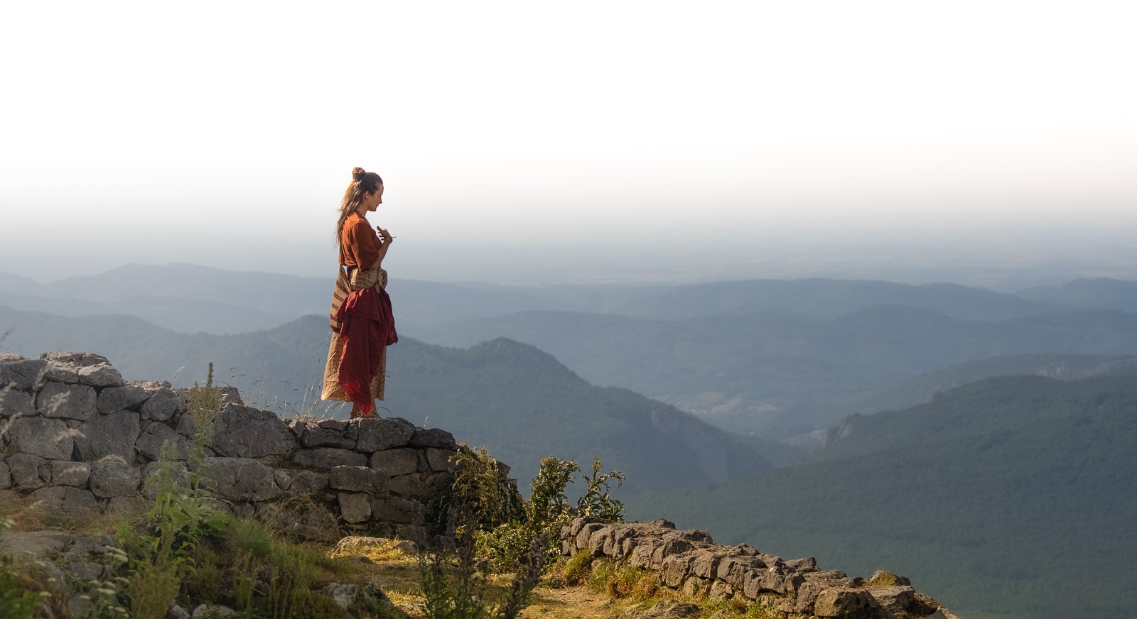 Woman standing on a stone wall above misty mountains