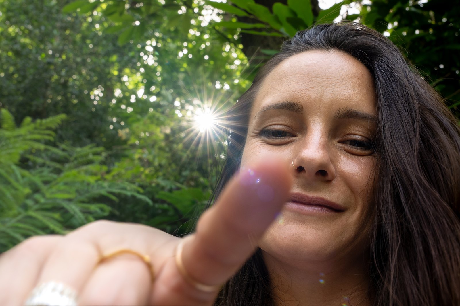 Woman in a sunlit forest pointing towards the camera