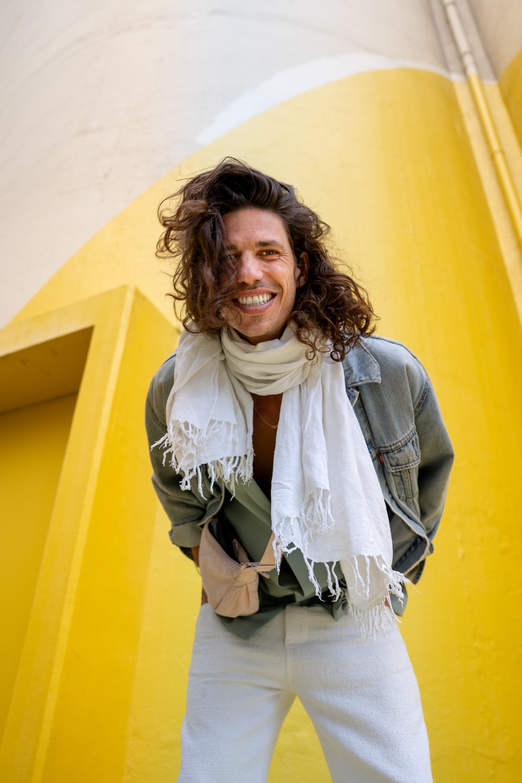 Smiling man with a white scarf against a yellow wall