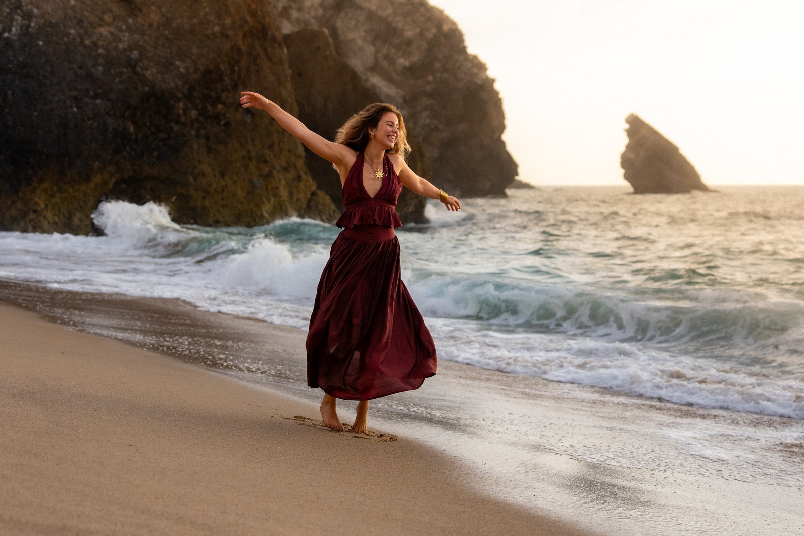 Woman in a red dress dancing on the beach by the rocks