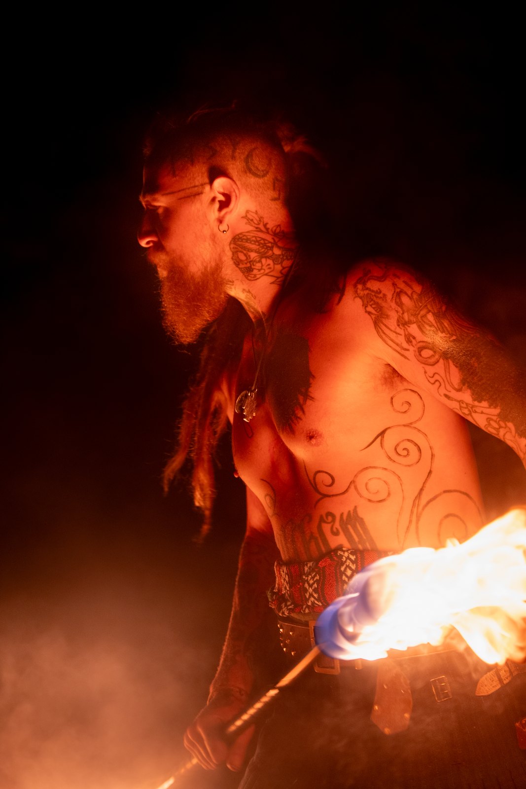 Fire performer with painted skin lit by a flaming torch at night
