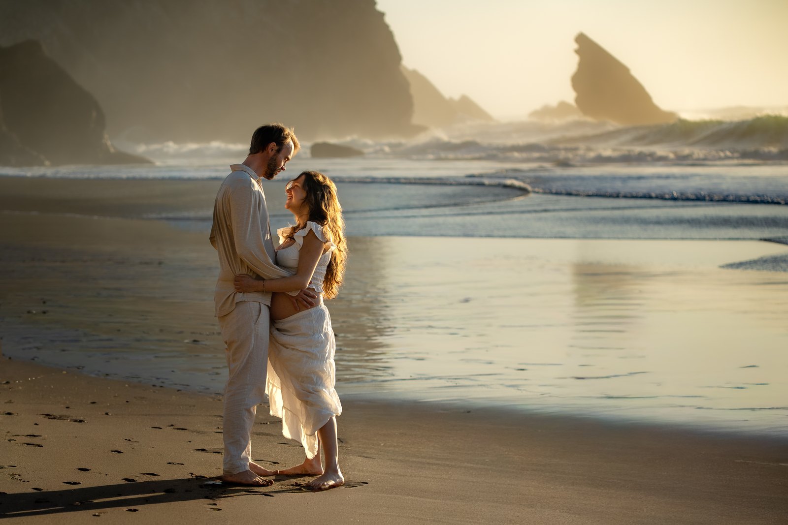 Expecting couple embracing on the beach at golden hour