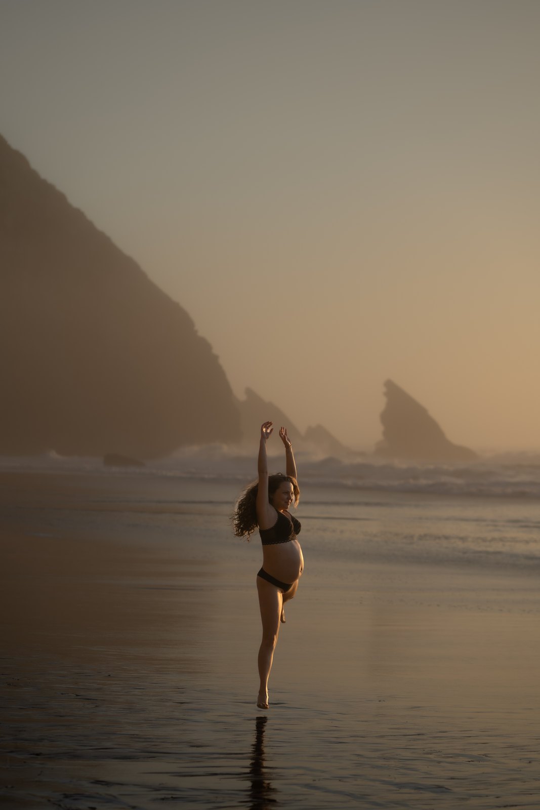 Pregnant woman stretching her arms to the sky by the sea