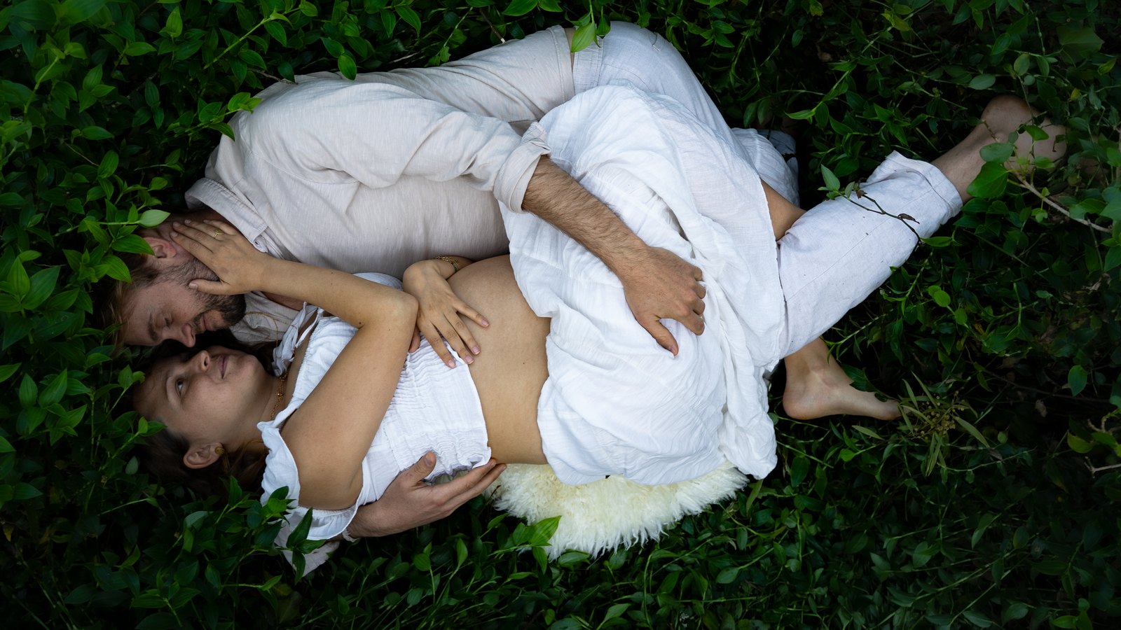 Couple lying on the grass, hands resting on her belly