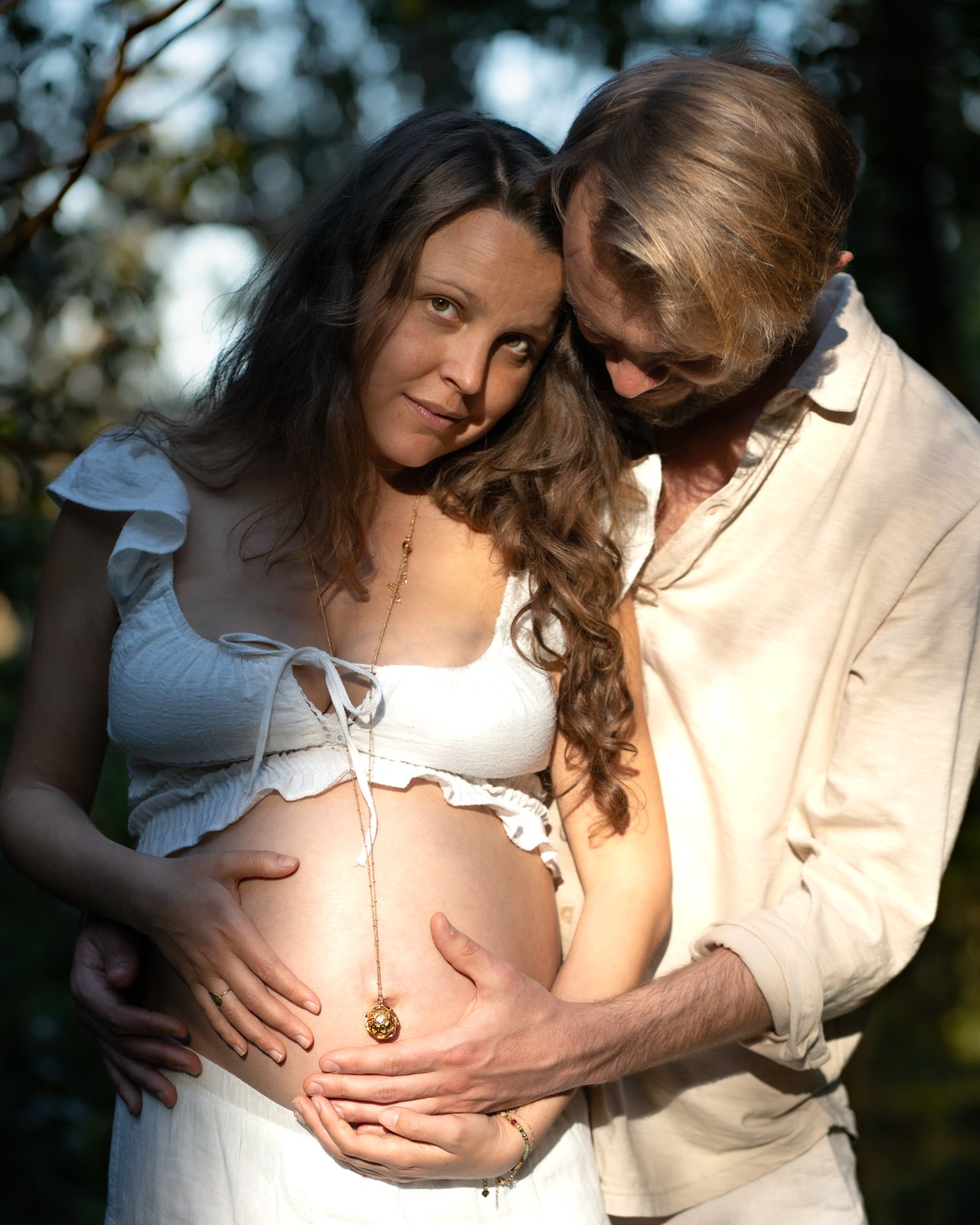 Partner holding the belly of an expecting mother in forest light